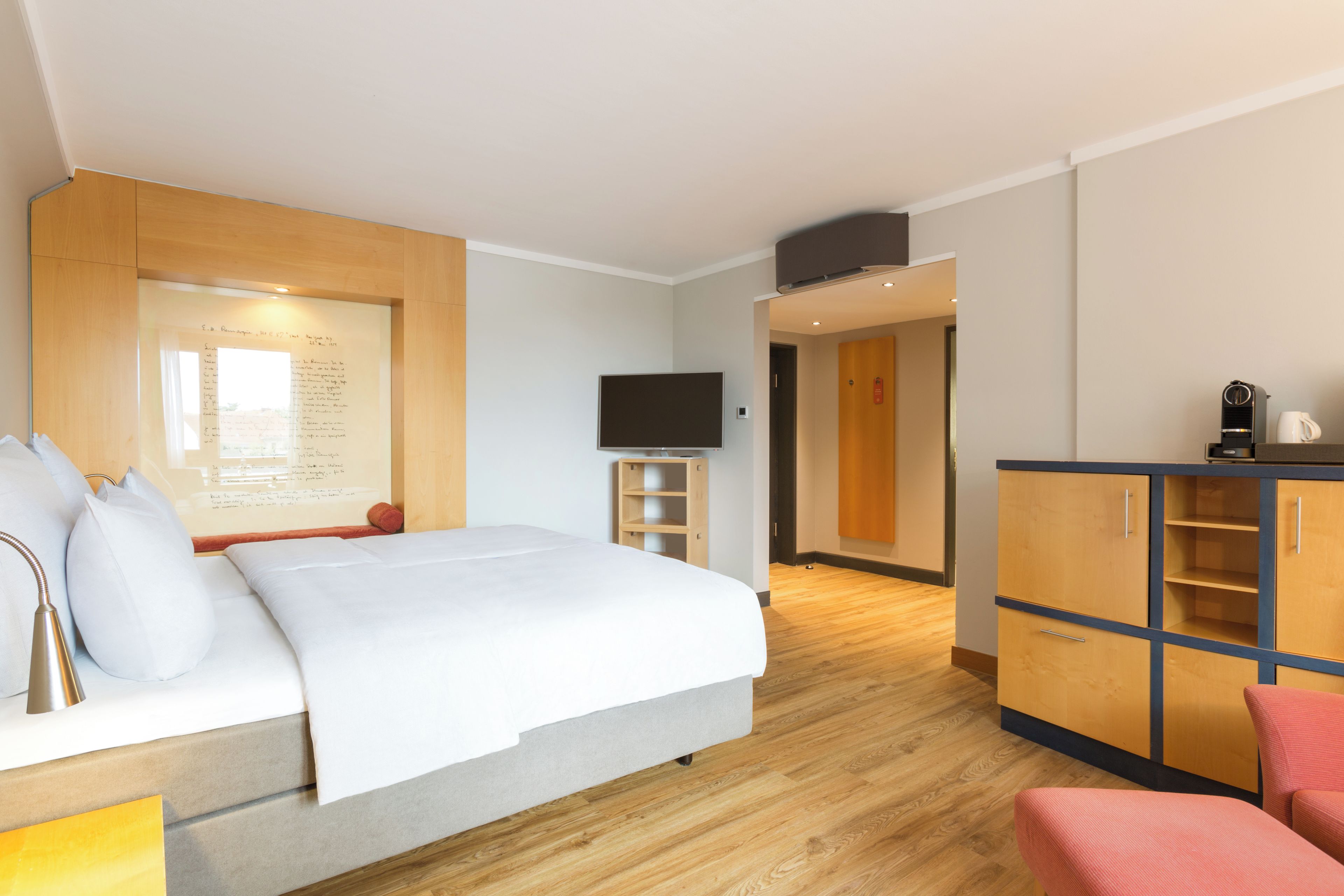 A hotel room with a bed, a television, a desk with a coffee machine, and a wardrobe.