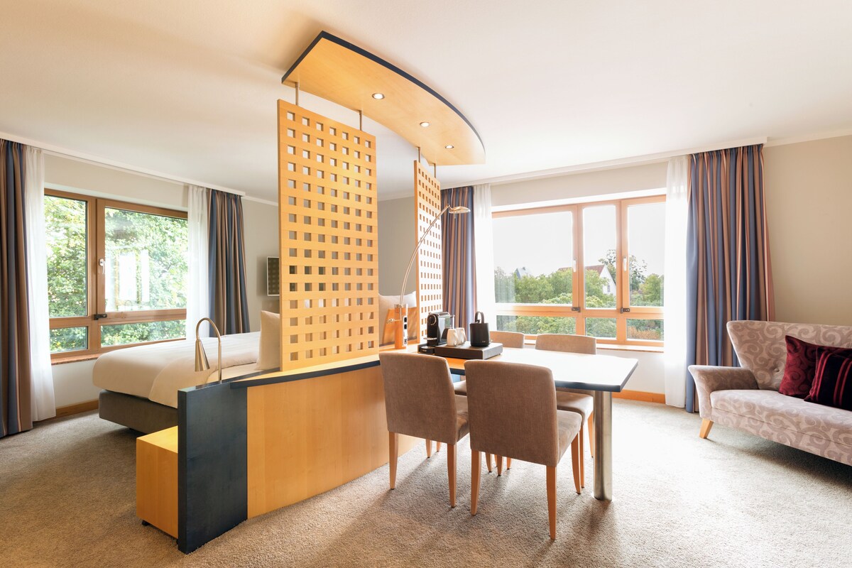 Una habitación de hotel con cama, escritorio con silla, sofá y ventanas amplias.