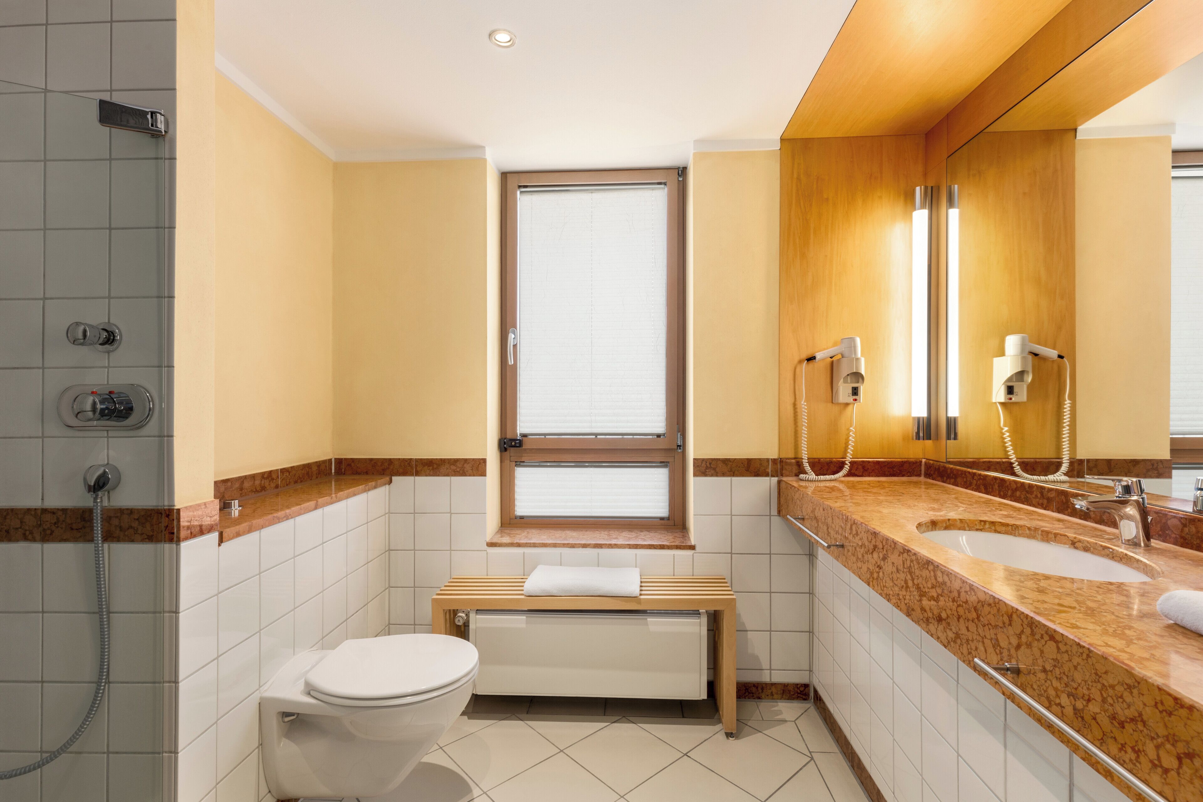 Une salle de bain comprenant des toilettes, un banc, un lavabo avec un miroir et une douche.