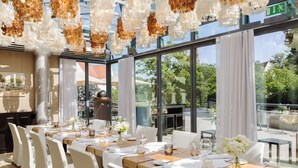 A restaurant with a long table set for dining, large windows, and hanging decorative elements. - Hotel Remarque (Osnabrueck)