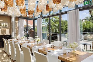 A restaurant with a long table set for dining, large windows, and hanging decorative elements.