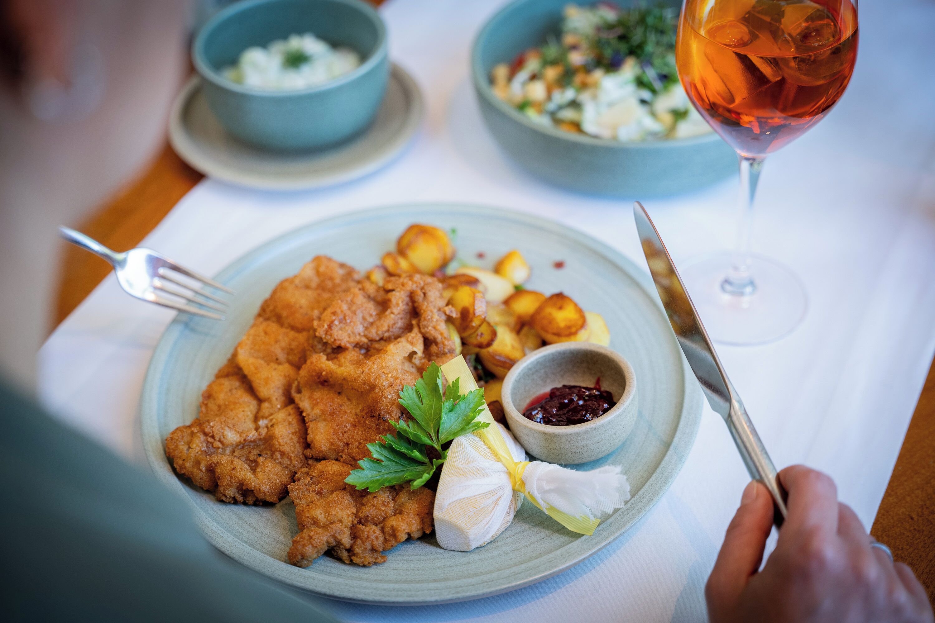 Une assiette de nourriture avec une fourchette et un couteau, un verre de boisson rouge et un saladier de salade.