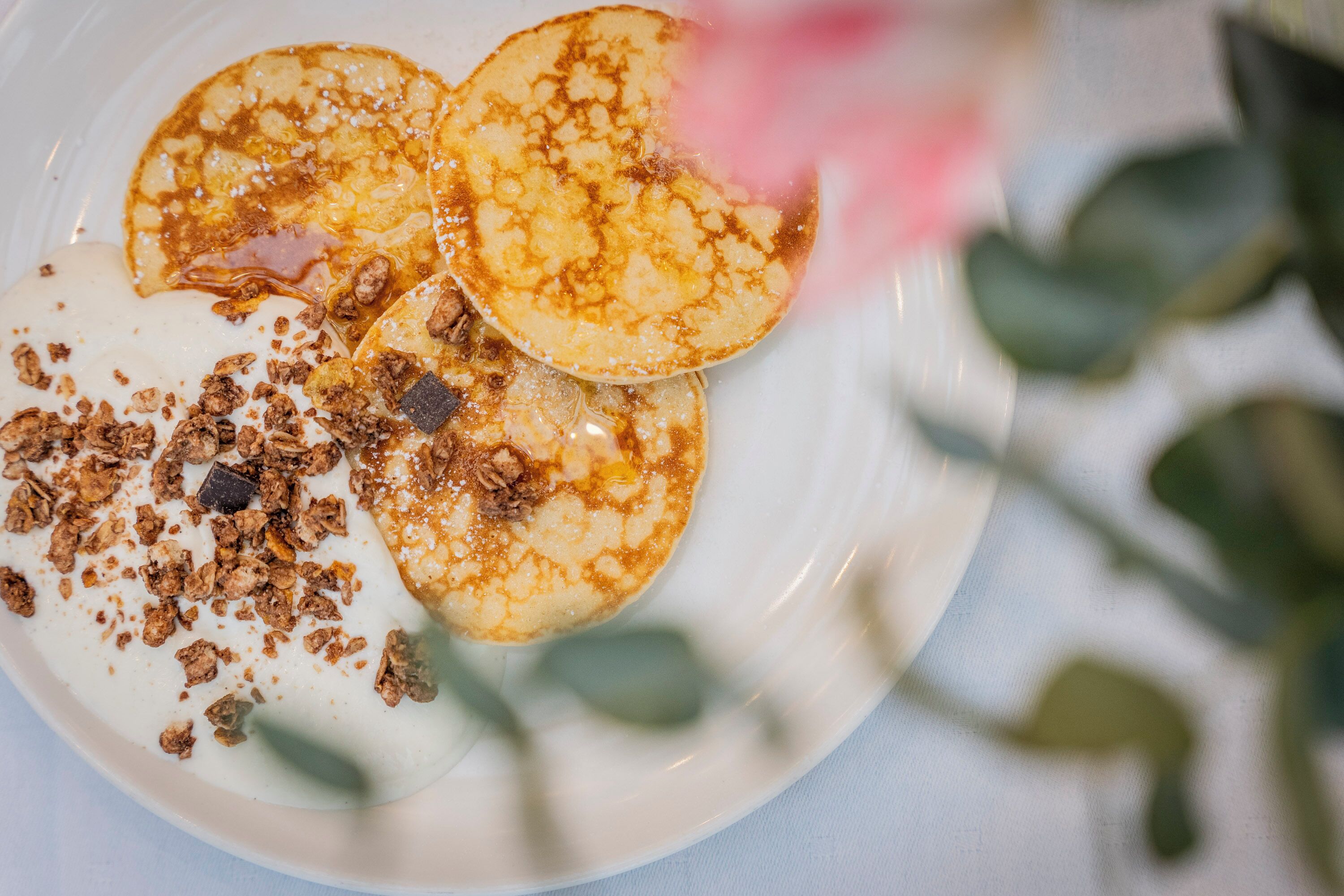 Ein Teller mit Pfannkuchen, Granola und einer rosa Blüte.