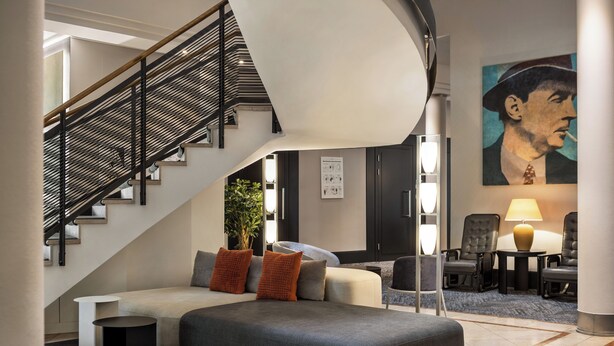 A modern hotel lobby with a staircase, seating area, and artwork.
