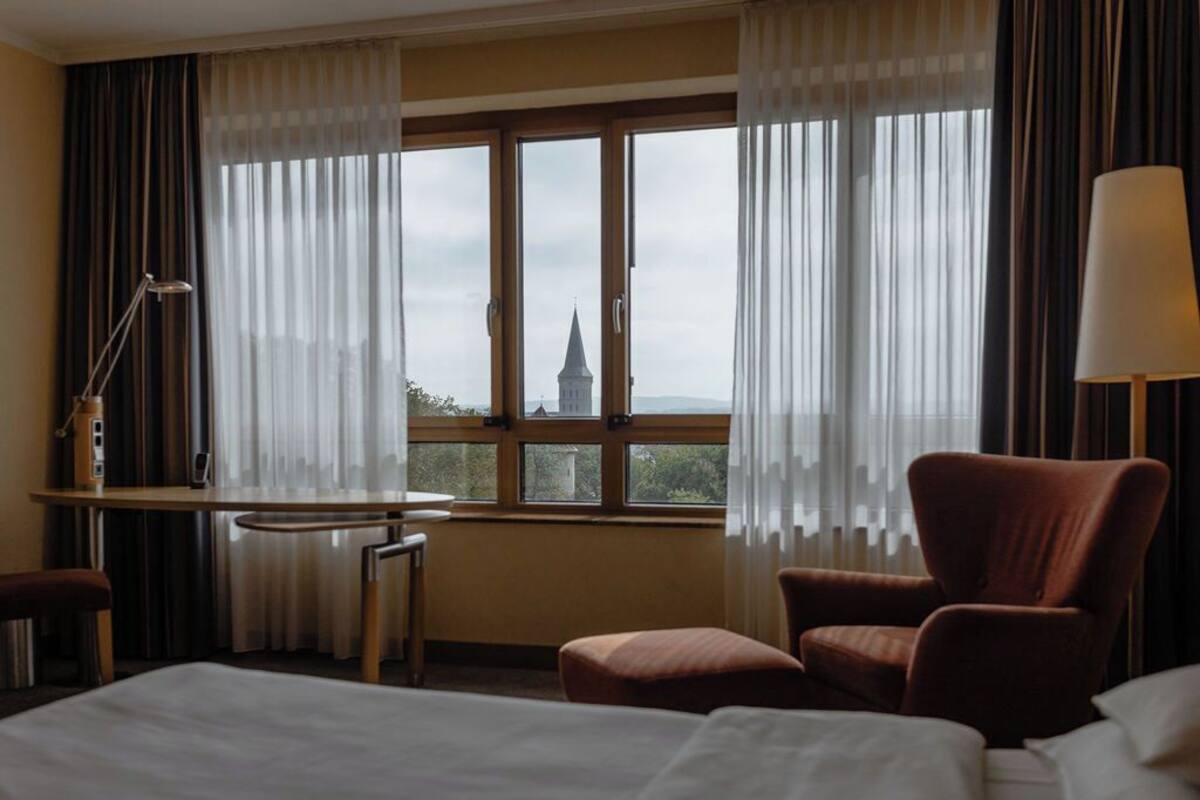 Habitación de hotel con cama, escritorio, silla y vista a una torre por la ventana.