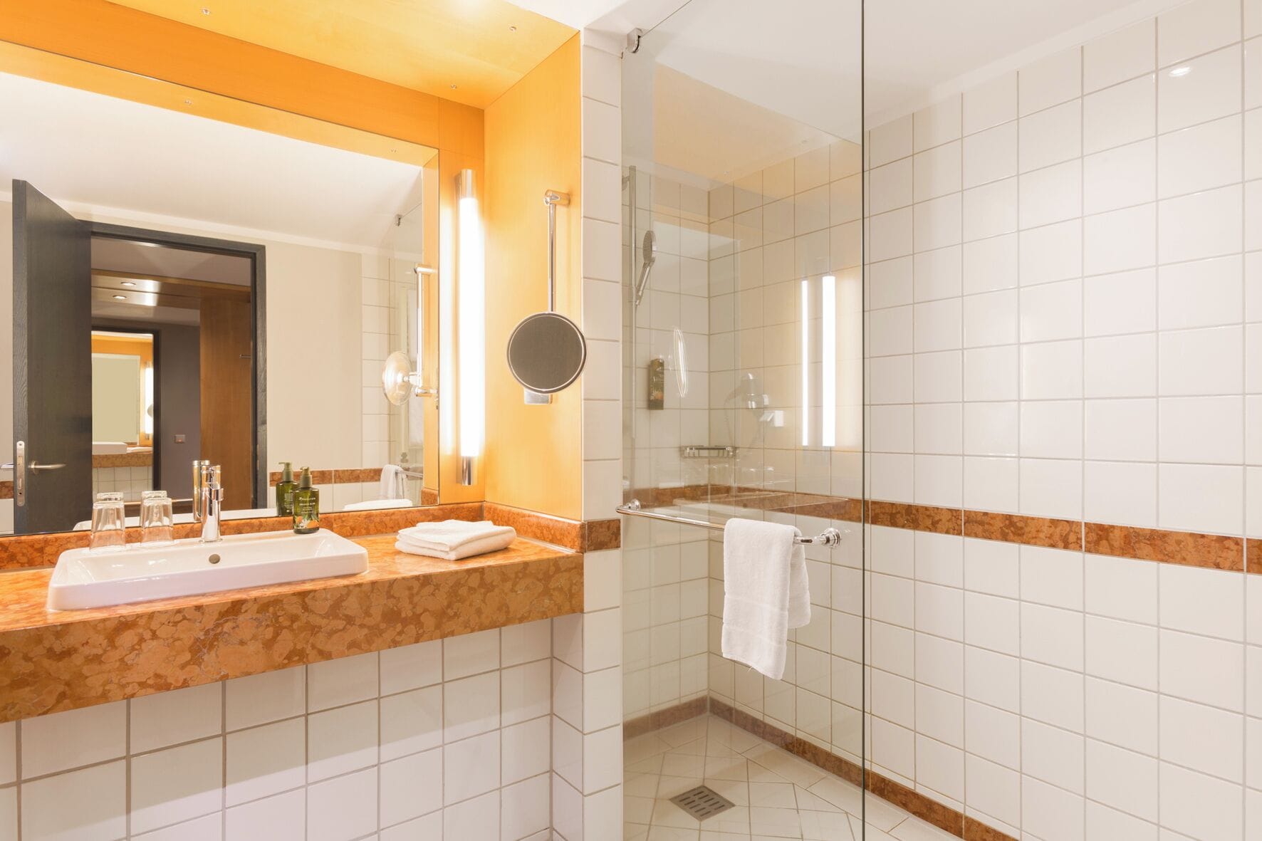 Un baño moderno con encimera de mármol, un espejo grande y cabina de ducha con paredes de vidrio.