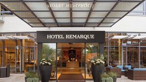 A hotel entrance with a glass facade, a sign reading 'HOTEL REMARQUE,' and potted plants at the entrance. - Hotel Remarque (Osnabrueck)