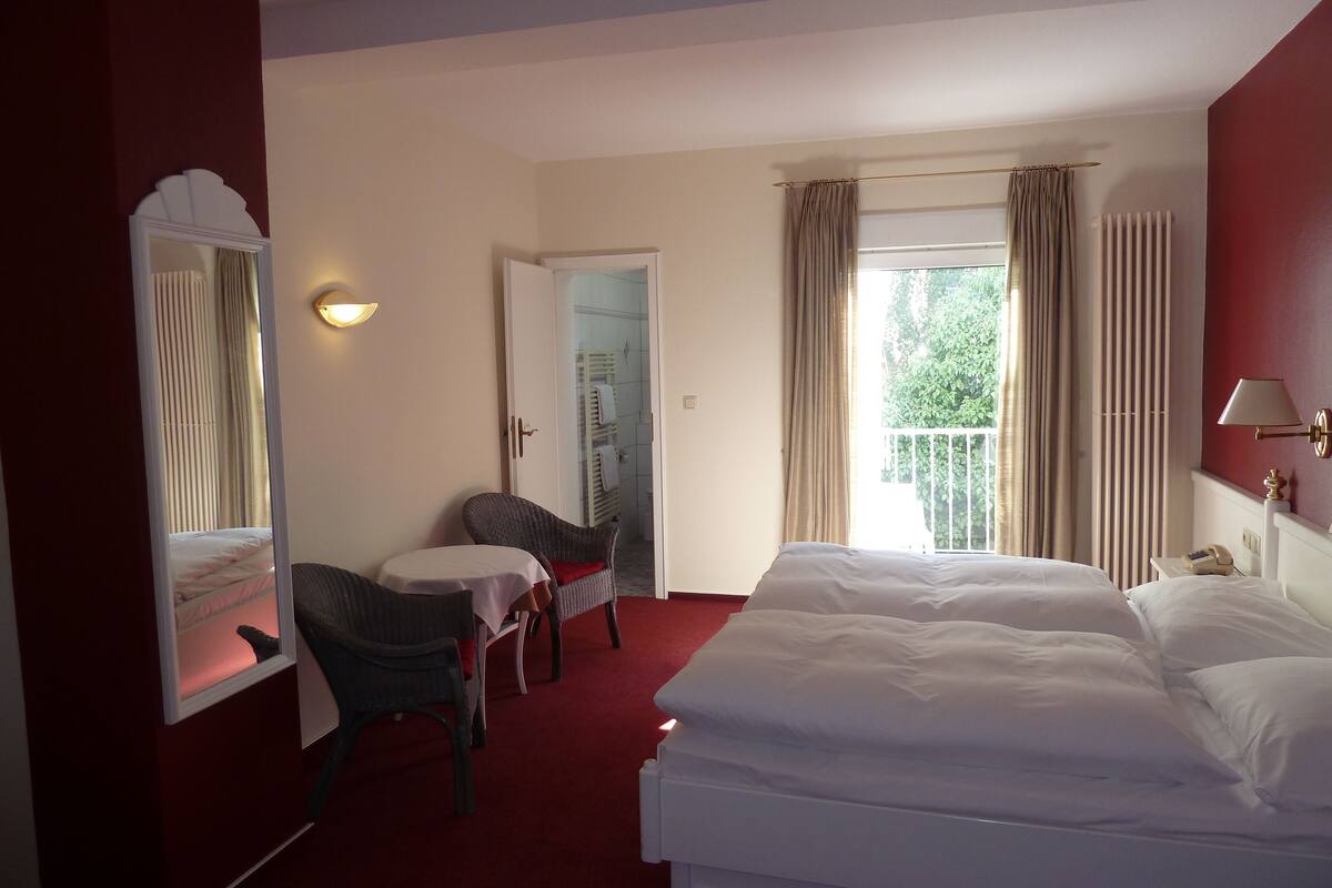 Una habitación de hotel con cama, una silla, una mesa, un espejo y una ventana con cortinas.