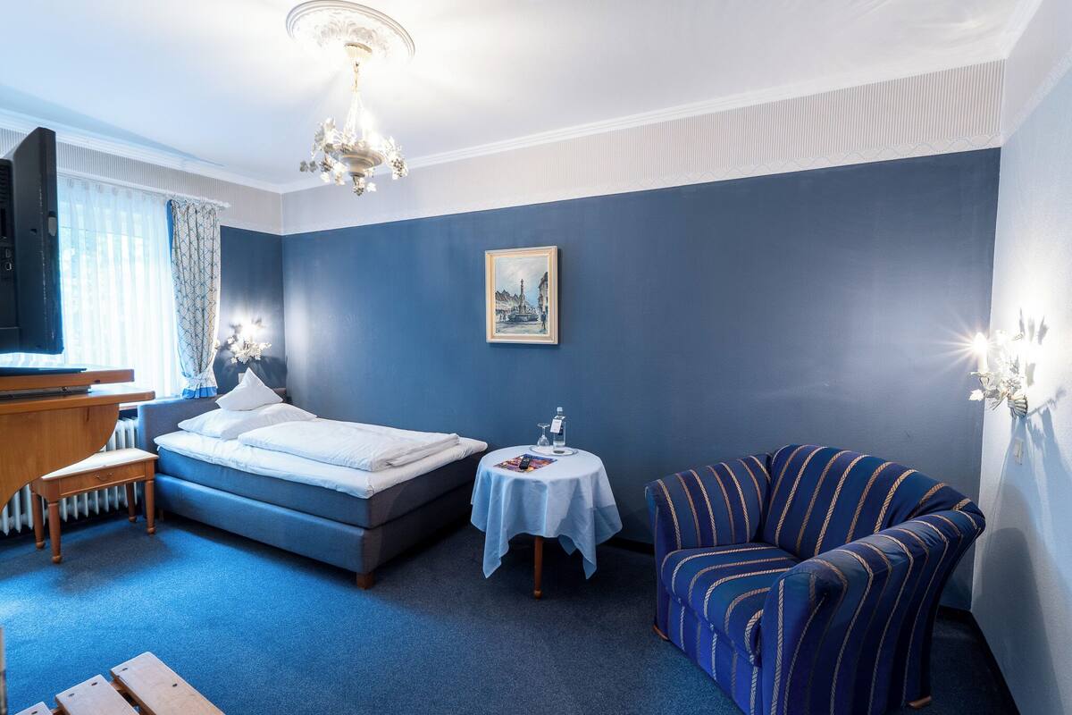 Un dormitorio con una cama, una mesita de noche con lámpara, una silla y un televisor.