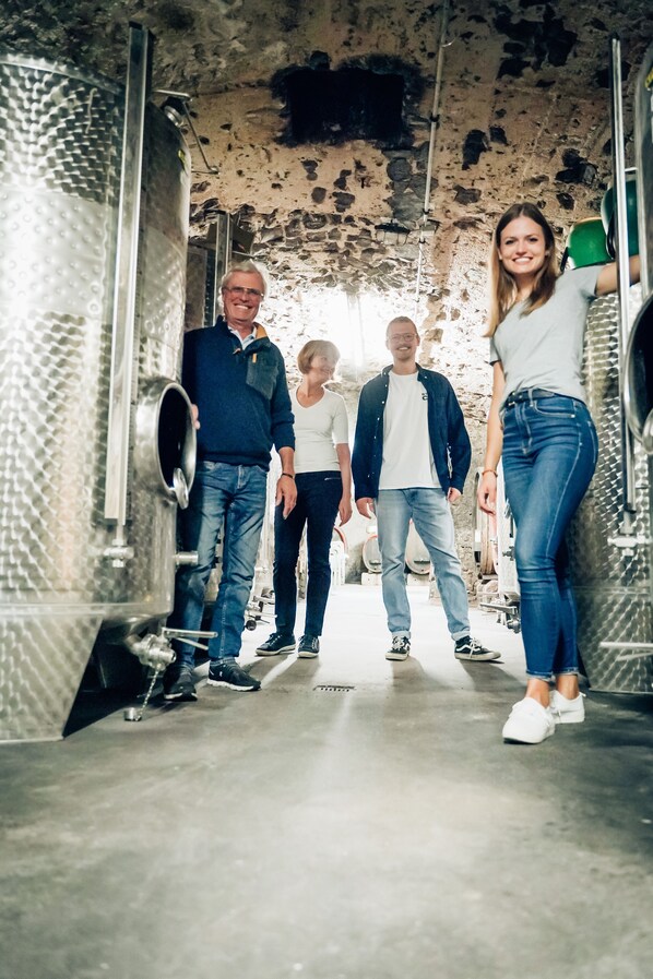 Un grupo de personas de pie en una habitación con tanques metálicos de estilo industrial y una pared de piedra tosca.