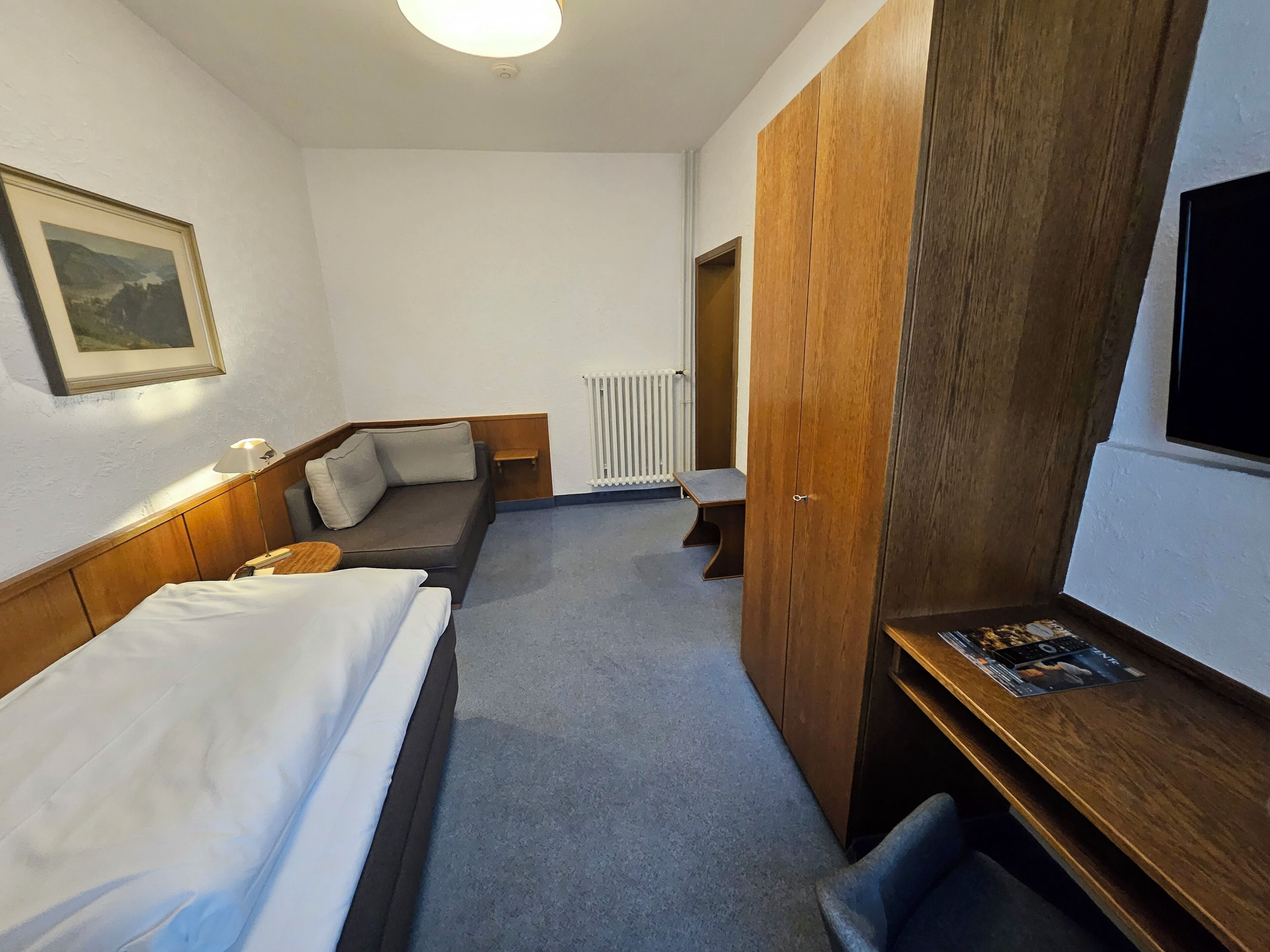 Ein Hotelzimmer mit Bett, einer Couch, einem Schreibtisch, einem Fernseher, einer Heizung und einem Holzschrank.