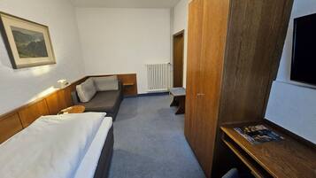 Ein Hotelzimmer mit Bett, einer Couch, einem Schreibtisch, einem Fernseher, einer Heizung und einem Holzschrank.