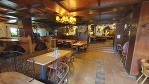 En restaurang med träbord och stolar, en bardisk och en trappa som leder till en annan del av lokalen.