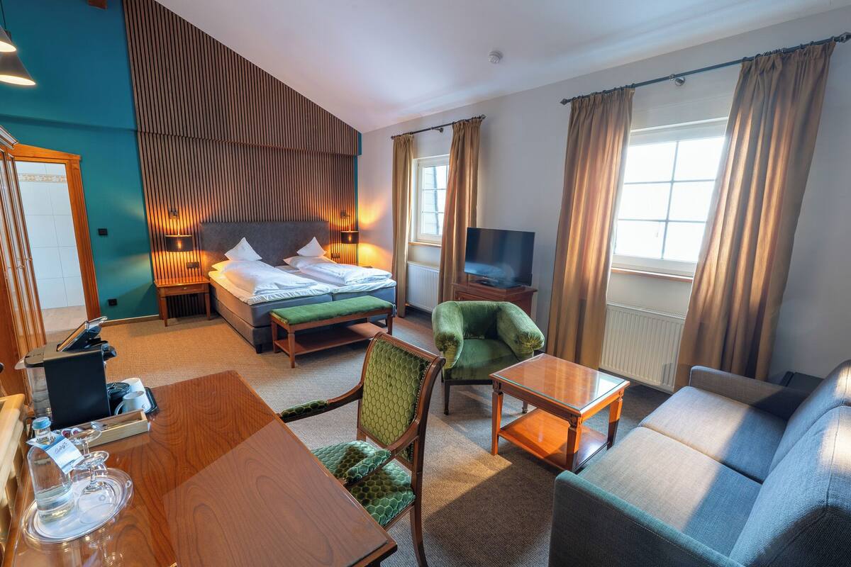 Una habitación de hotel con cama, televisor, sofá, sillón, mesa y escritorio.