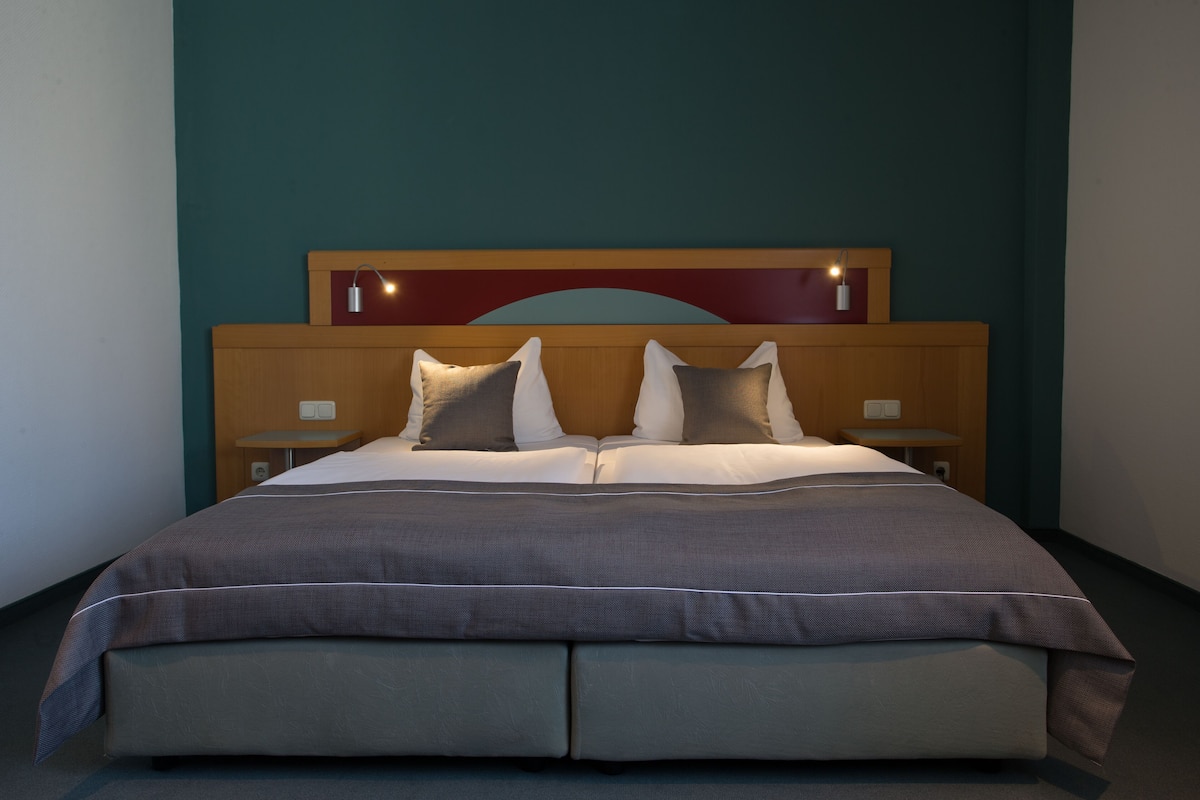 A neatly made bed with a headboard, two bedside tables, and a wall-mounted light fixture.
