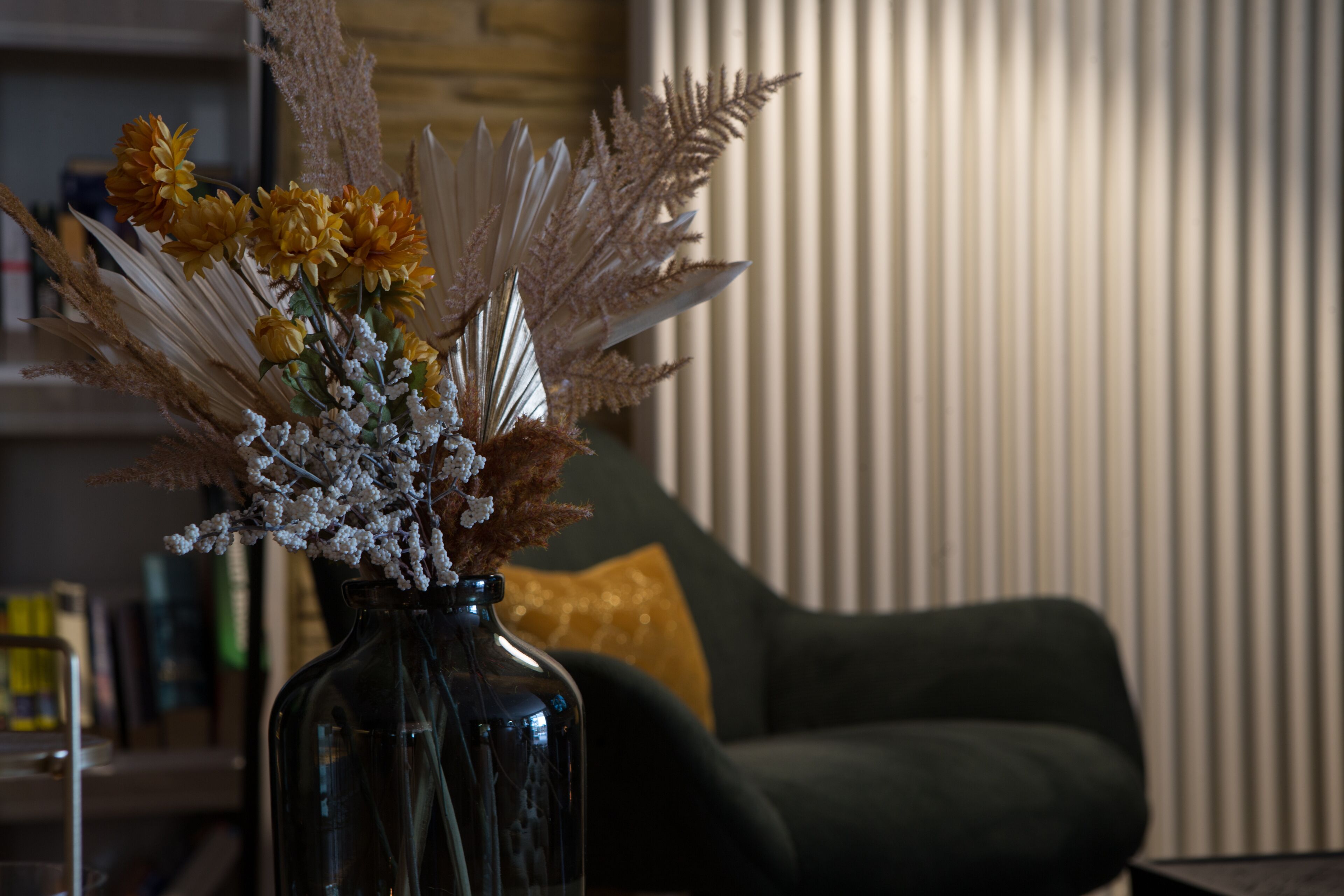 Un jarrón con flores y plantas secas sobre una mesa en una habitación con un sofá y una pared a rayas.