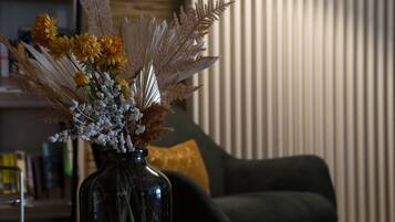 Un jarrón con flores y plantas secas sobre una mesa en una habitación con un sofá y una pared a rayas.