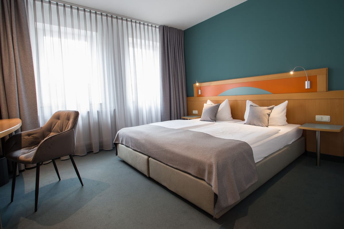 A hotel room with a large bed, a chair, a small table, and a nightstand.