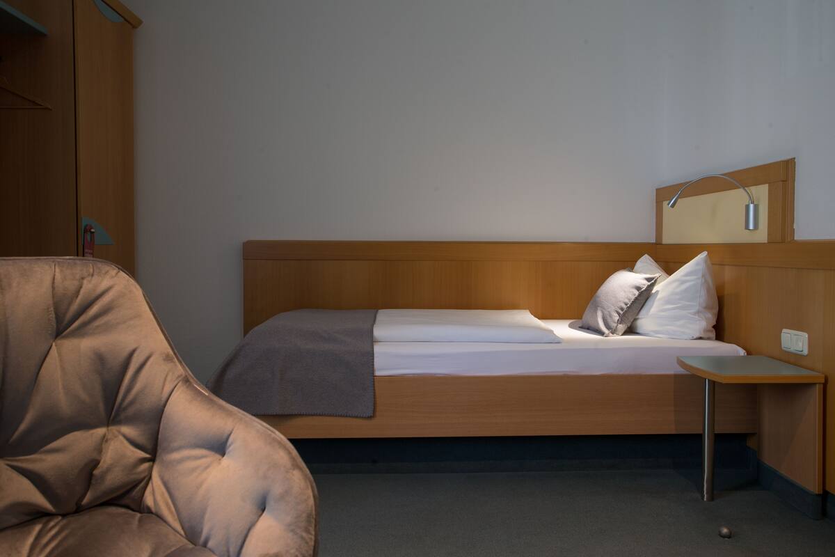 A bedroom with a wooden bed, a small bedside table, a chair, and a wardrobe.