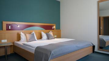 Una habitación de hotel con una cama de madera, una mesita de noche, un espejo y una pared color esmeralda.