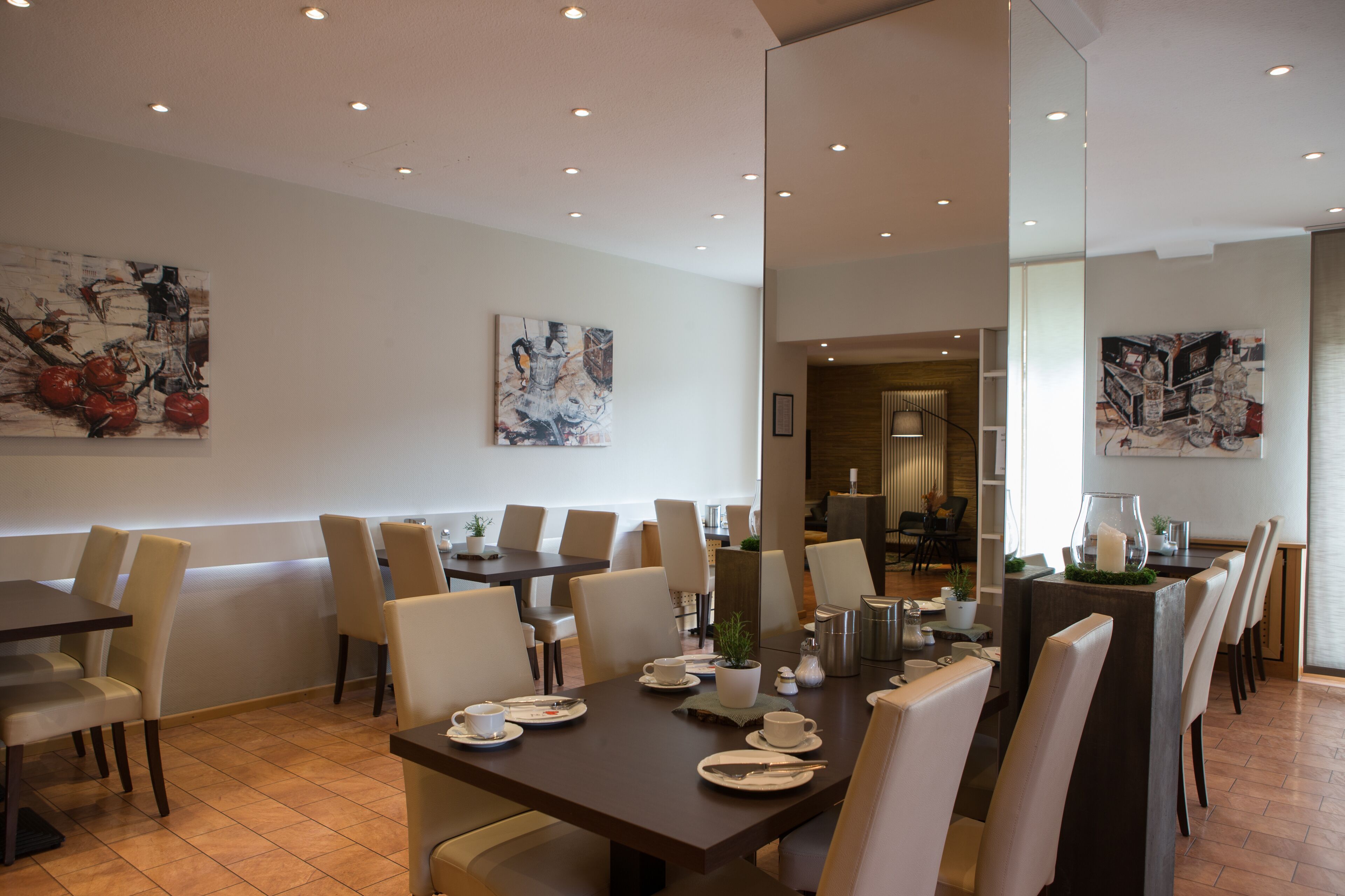 A modern dining area with multiple tables and chairs, artwork on the walls, and a well-lit ceiling.