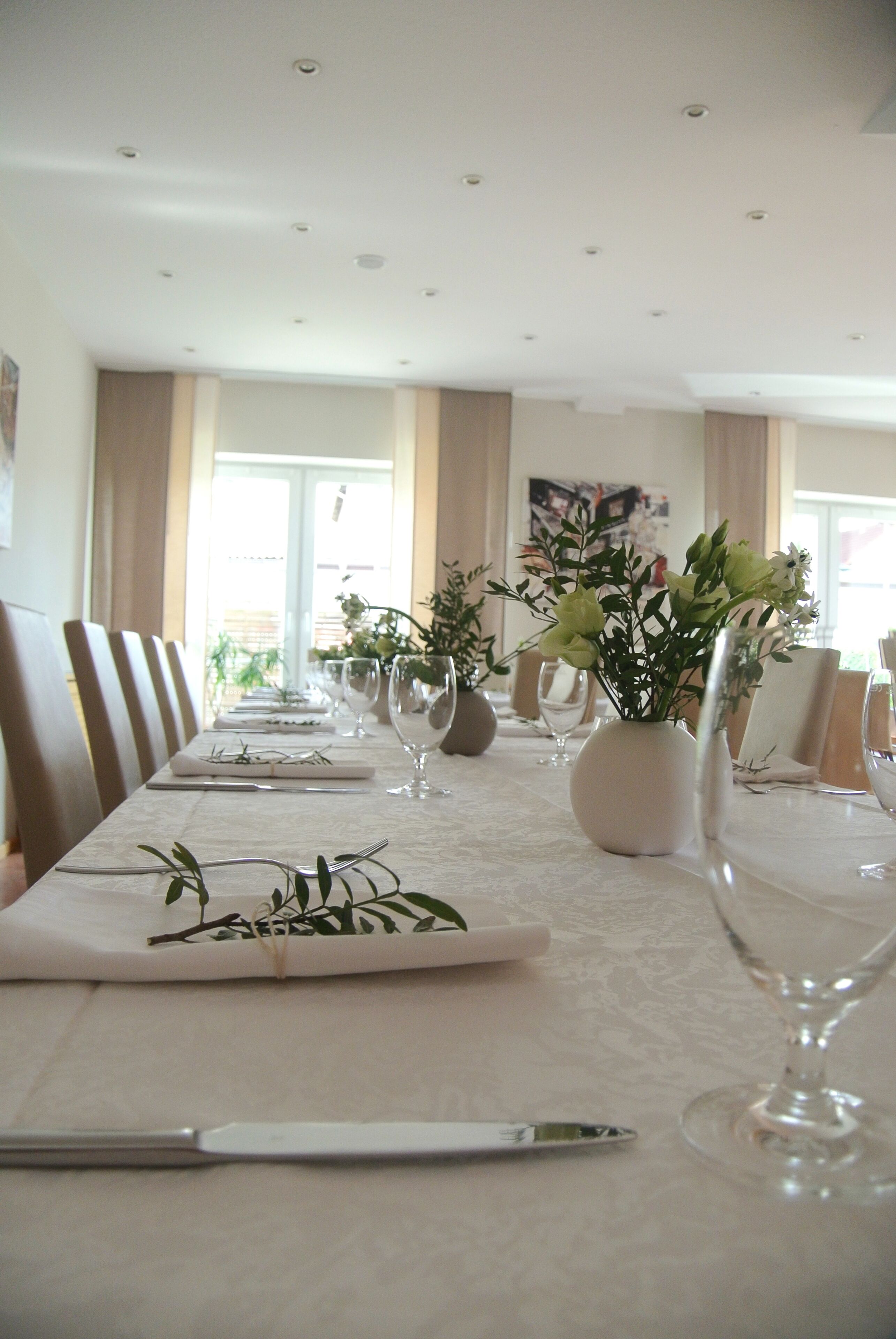 A long dining table set with white tablecloth, plates, cutlery, and vases with flowers.