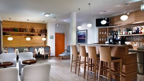 Uma área de bar moderna, com cadeiras de madeira, balcão e uma televisão montada acima.