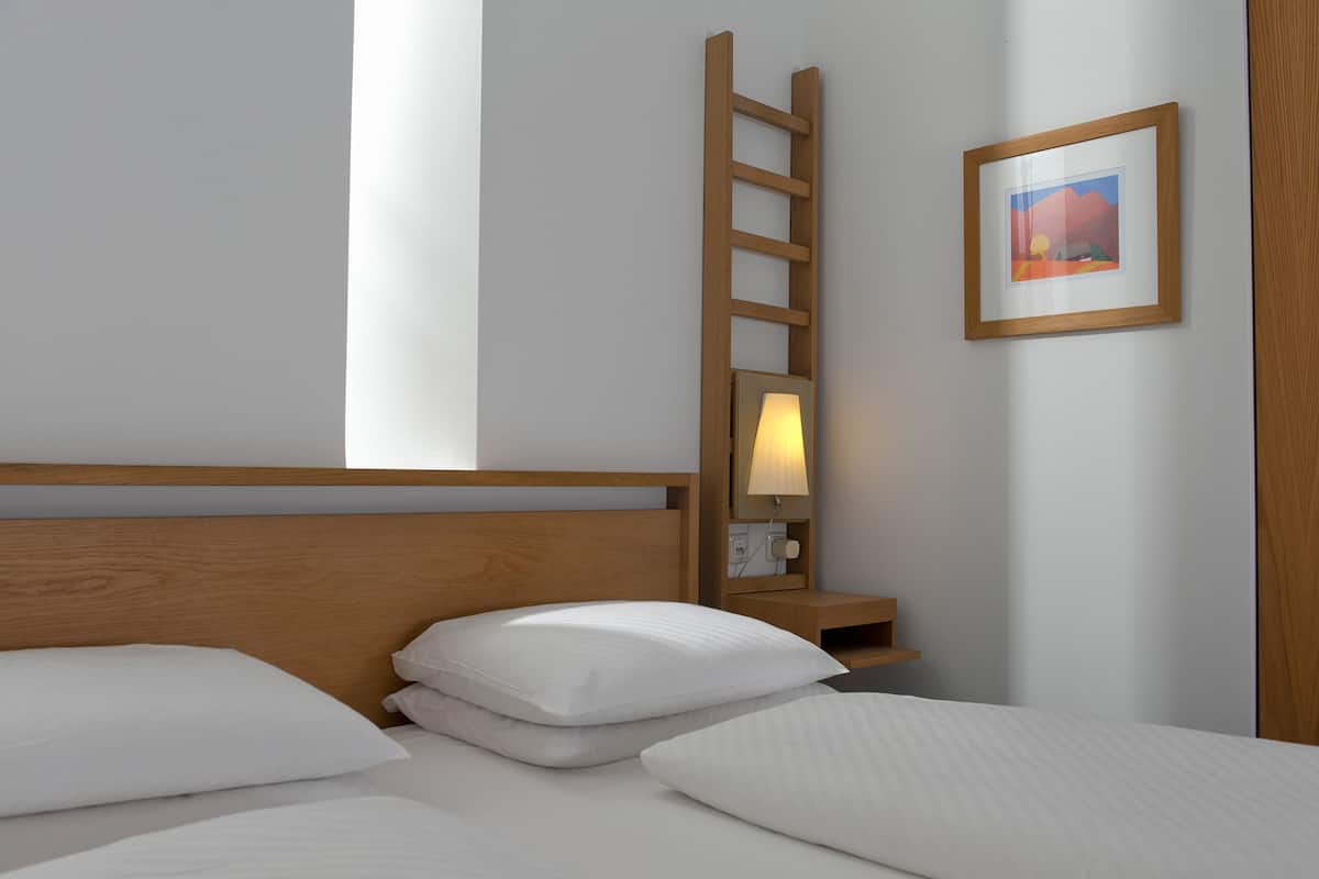 A neatly made bed with white linens and pillows, a wooden ladder leaning against the wall, and a framed picture on the wall.