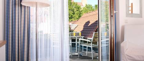 A room with a sliding glass door leading to an outdoor patio with a table and chairs, a lamp, and a view of a building with a tower.