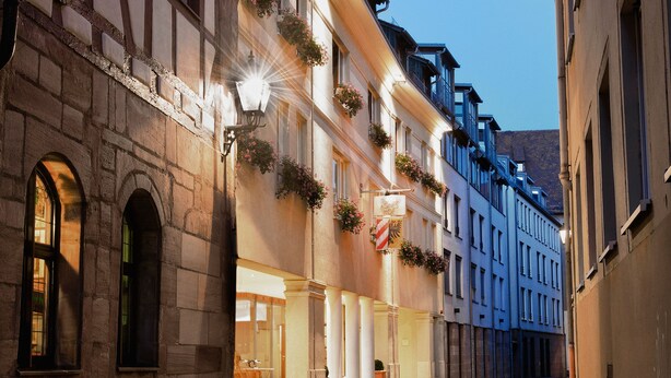 Uma rua de paralelepípedos ladeada por edifícios históricos, alguns com caixas de flores e toldos.