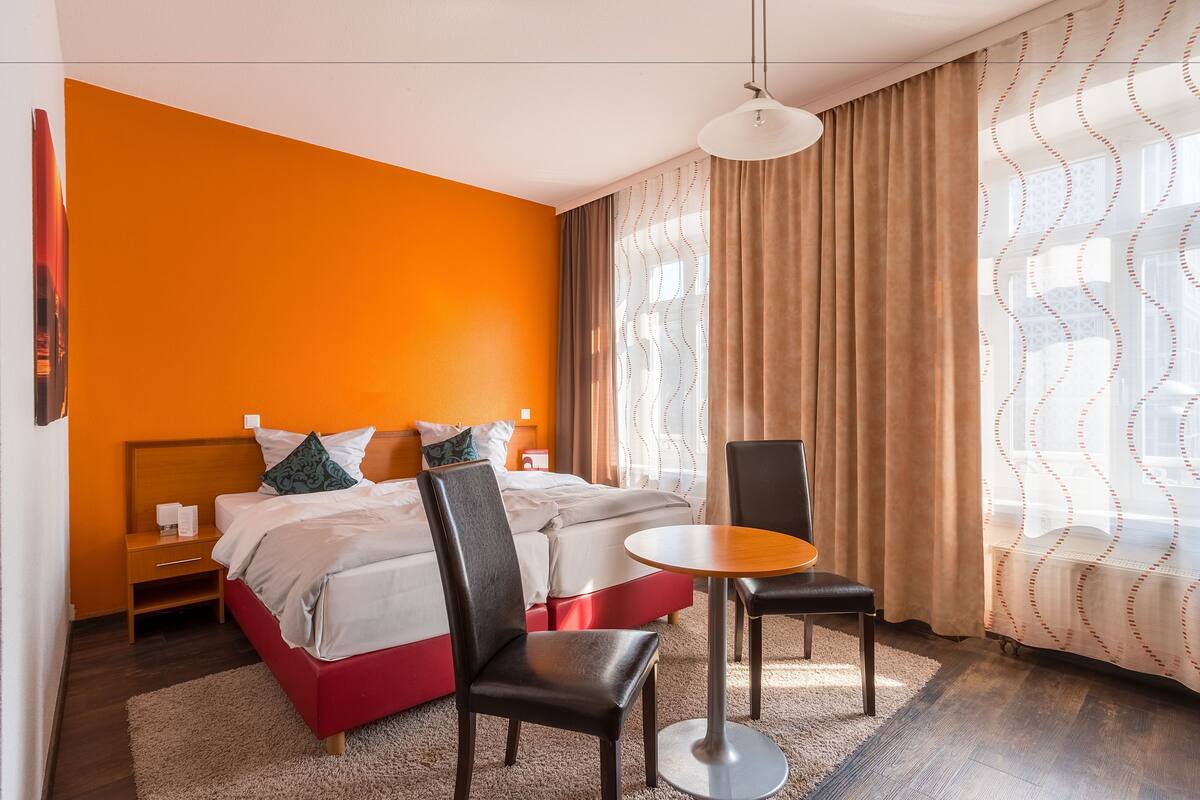 A hotel room with a bed, two chairs, a small table, and a window with curtains.