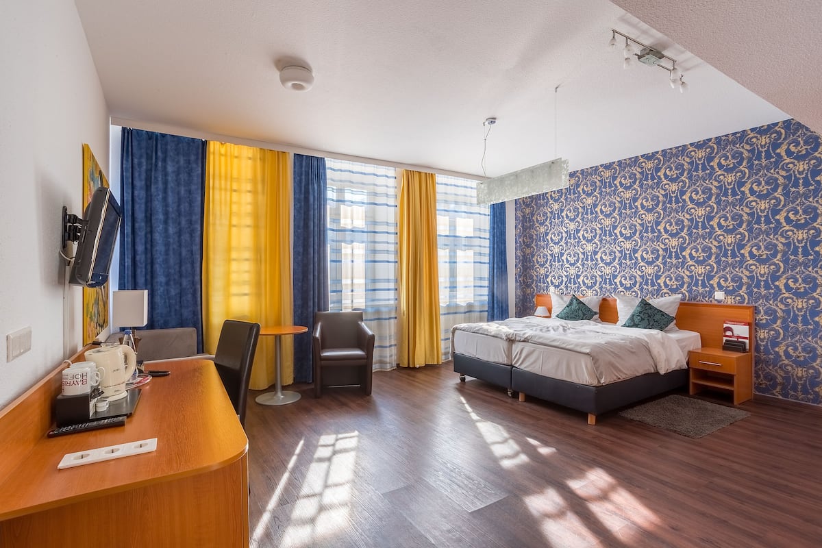 A hotel room with a bed, a desk, a chair, a small table, and a nightstand.