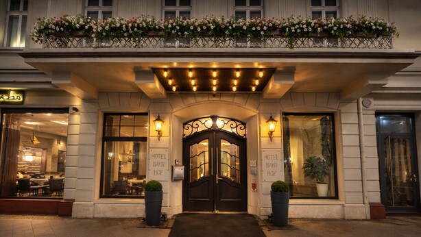 A hotel entrance with a dark wooden door, two potted plants, and a balcony with flowers. - Hotel Bayrischer Hof (Heidelberg)