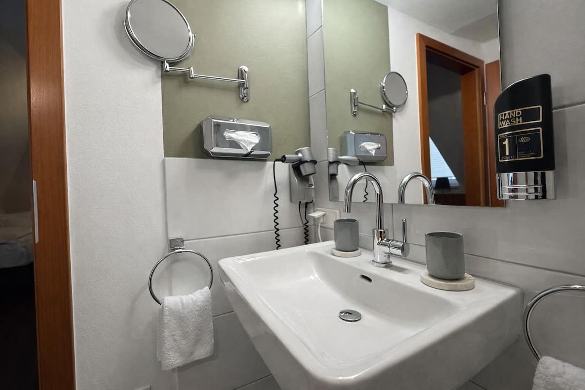 A modern bathroom with a white sink, two faucets, a mirror, and a hand wash station.