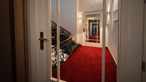 A hallway with a red carpet, a black spiral staircase, and a white door. - Hotel Bayrischer Hof (Heidelberg)