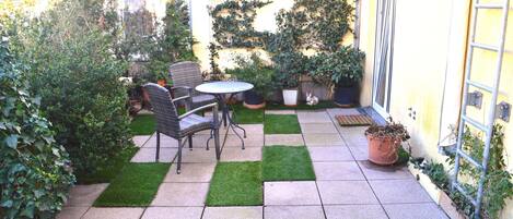 A patio with a table and chairs, surrounded by potted plants and a small lawn area.