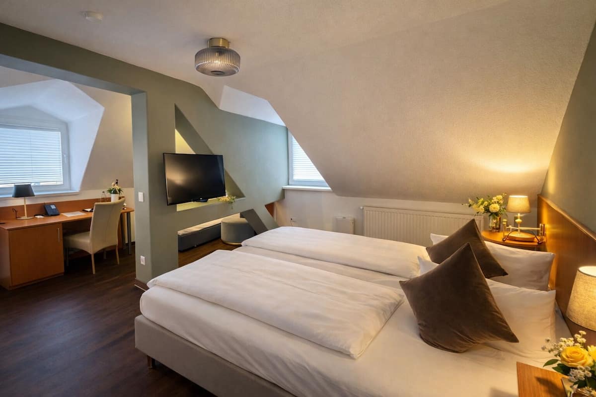 A modern hotel room with a large bed, a desk, a TV, and a skylight.