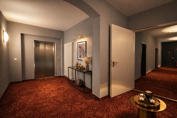 A hallway with a patterned carpet, a glass console table with decorative items, and a door leading to another room. - Hotel Bayrischer Hof (Heidelberg)