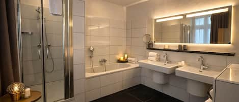 A modern bathroom with a glass-enclosed shower, a bathtub, two sinks, a toilet, and a vanity with a mirror.