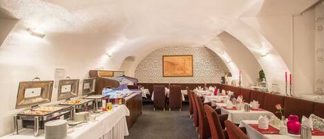 A dining area with buffet-style food stations, tables set with white tablecloths, and red upholstered chairs.