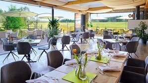 Un área de comedor al aire libre con varias mesas y sillas, sombrillas grandes y plantas en macetas.