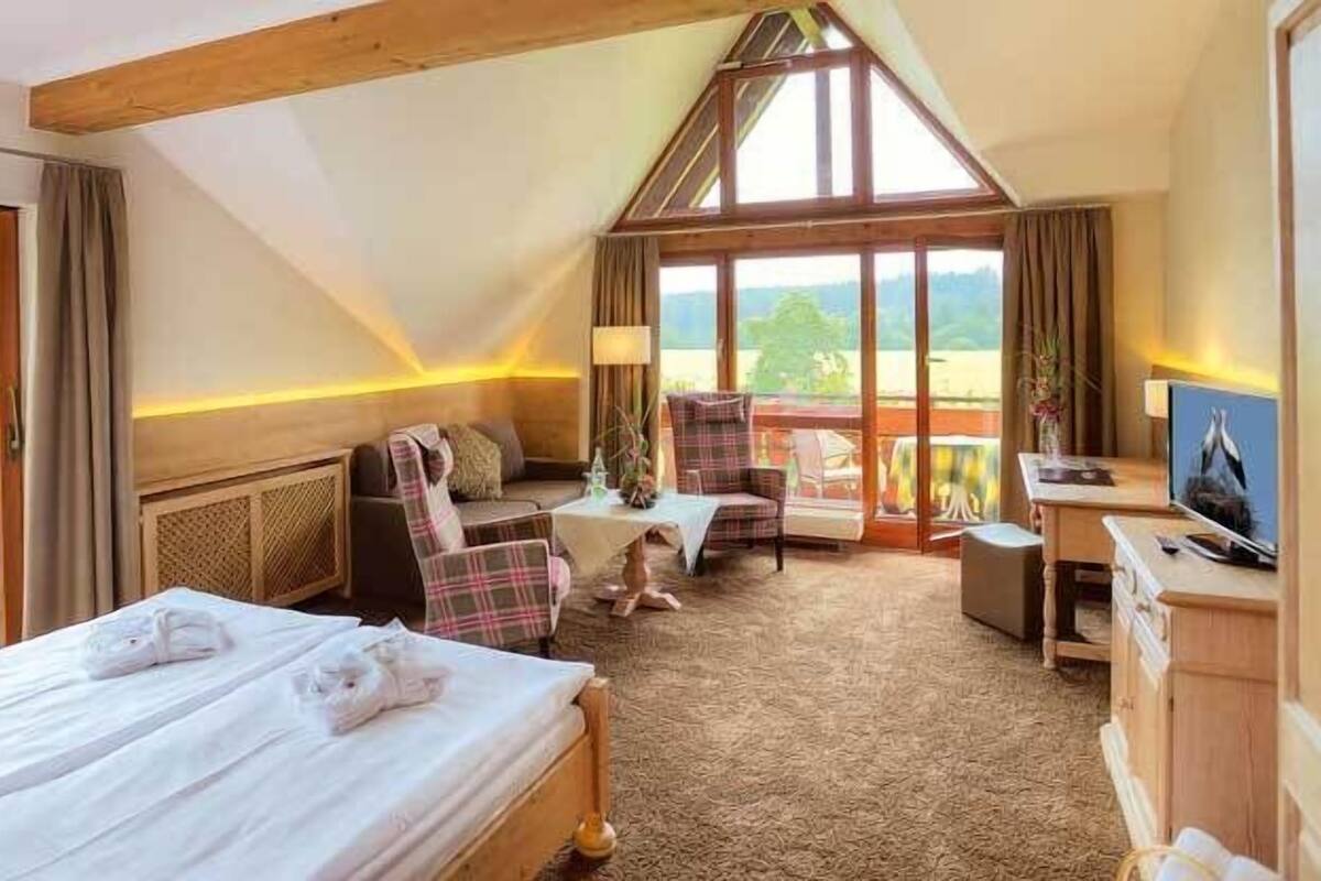 A hotel room with a large bed, a sofa, a TV, and a balcony with a view of the countryside.