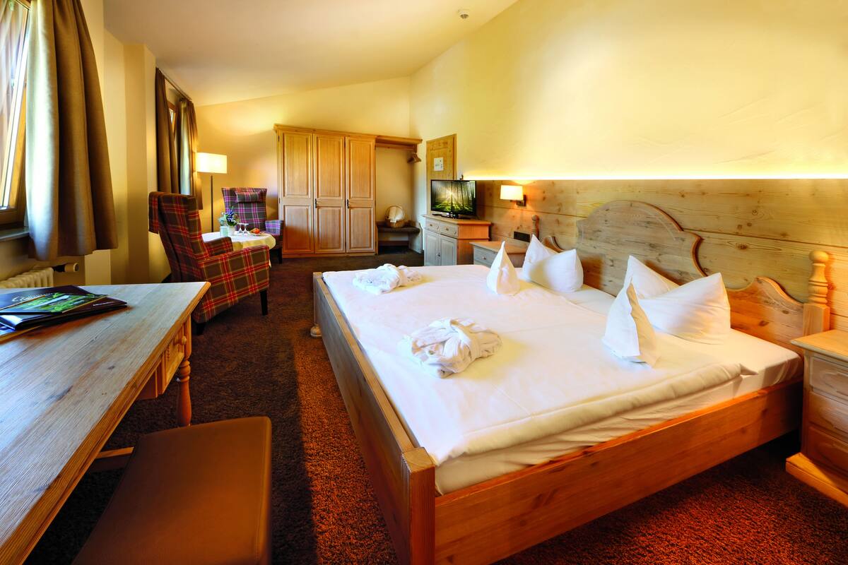 A hotel room with a wooden bed, a desk with a laptop, a chair, a television, and a wardrobe.