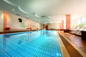 A large indoor swimming pool with tiled walls and ceiling, surrounded by lounge chairs and a sunlit area. - Hotel Grüner Wald (Freudenstadt)