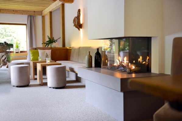 A modern living room with a fireplace, a sofa, ottomans, and a coffee table. - Hotel Grüner Wald (Freudenstadt)