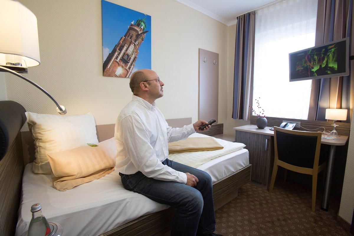 A hotel room with a bed, a desk, a television, and a bottle of water.