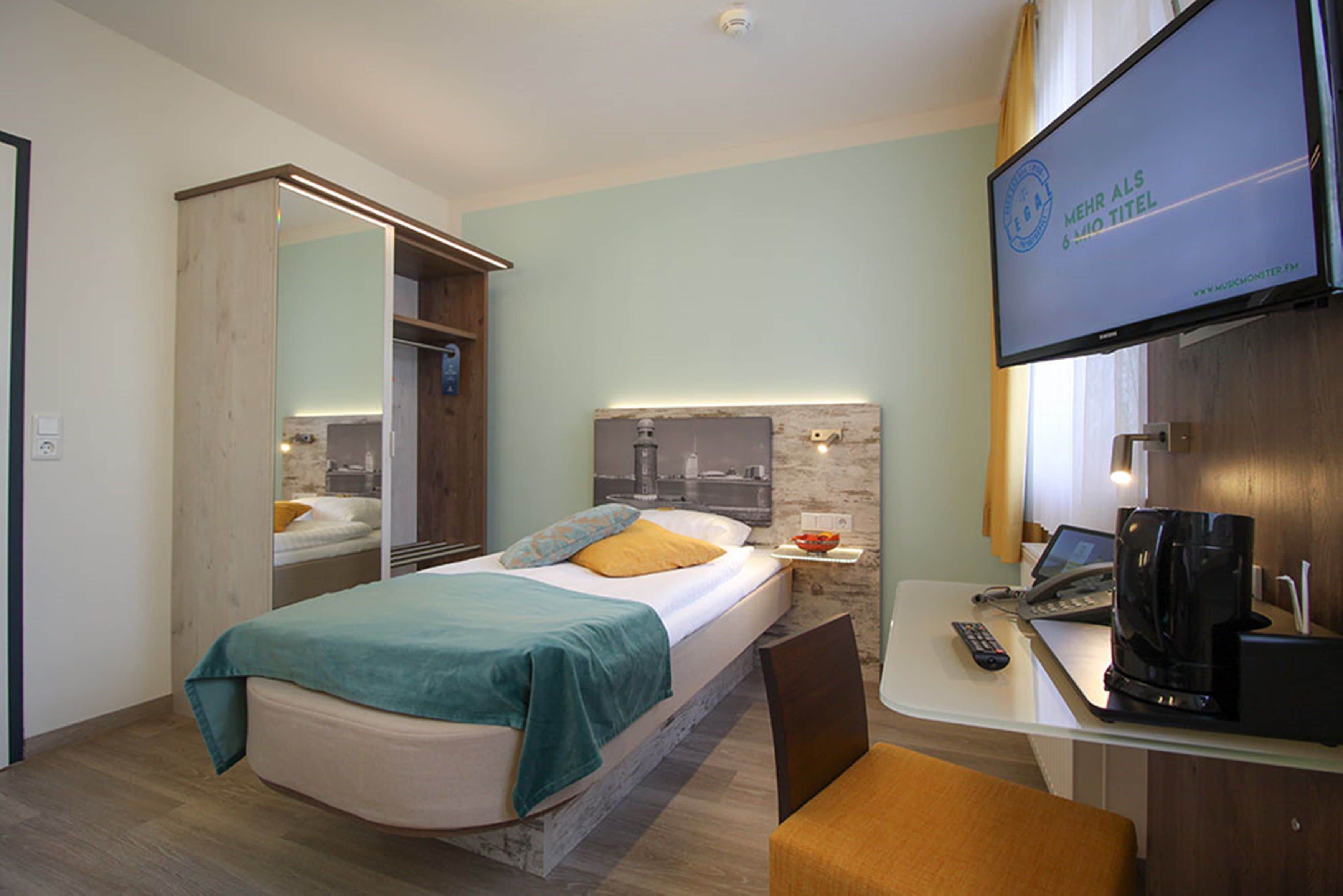 Una habitación de hotel con una cama, un escritorio con una computadora portátil, una cafetera y un televisor.