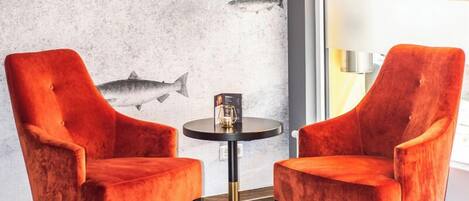 Une pièce avec deux fauteuils en velours rouge, une petite table ronde, un lustre doré et une fresque murale représentant des poissons.