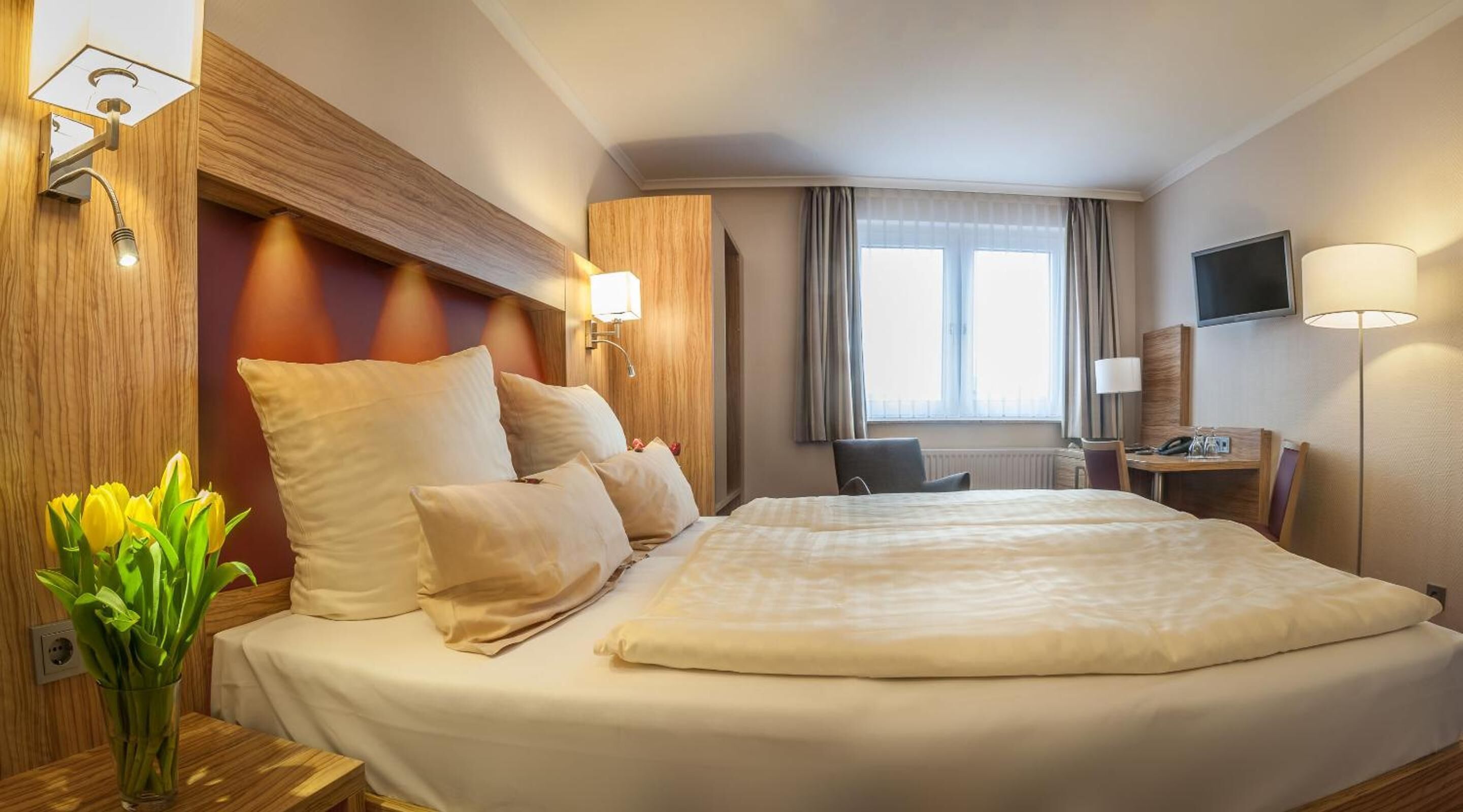 Une chambre d’hôtel avec un grand lit, un bureau avec une chaise, une télévision et une fenêtre avec des rideaux.