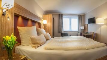 Une chambre d’hôtel avec un grand lit, un bureau avec une chaise, une télévision et une fenêtre avec des rideaux.